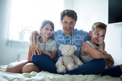 Portrait of father and kids sitting in bedroom