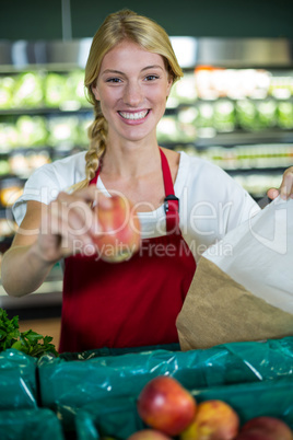Smiling female staff packing fruits in paper bag at supermarket