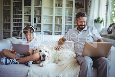 Father and son sitting on sofa and using digital tablet and laptop