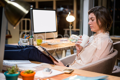 Businesswoman using digital tablet and holding coffee cup at her desk