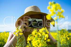 Woman taking picture from camera in mustard field
