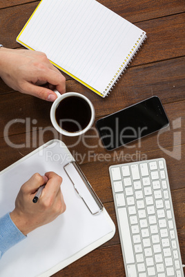 Man writing on clipboard while having cup of coffee