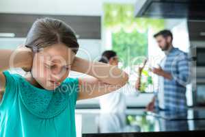 Sad girl covering her ears while parents arguing in background