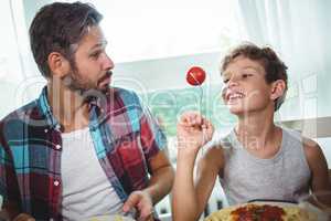 Smiling boy showing a cherry tomato to his father