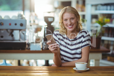 Portrait of woman using mobile phone while having cup of coffee