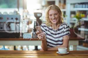 Portrait of woman using mobile phone while having cup of coffee