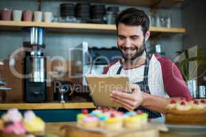 Smiling waiter using digital tablet in cafe