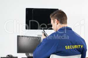 Security officer talking on walkie-talkie while looking at computer monitors