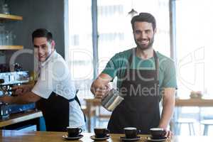 Smiling waiter making cup of coffee at counter in cafe