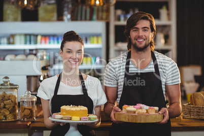 Portrait of waiter and waitress holding a tray of cupcakes