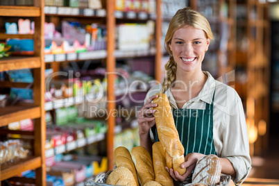 Smiling female staff holding loaf of bread at bread counter