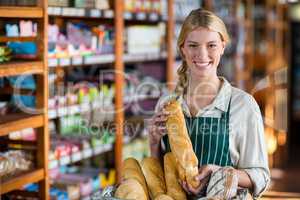 Smiling female staff holding loaf of bread at bread counter