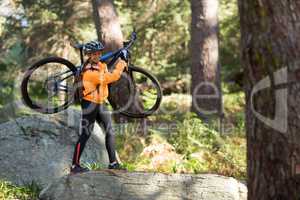 Female biker holding mountain bike and walking in forest
