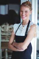 Portrait of smiling waitress standing with arms crossed