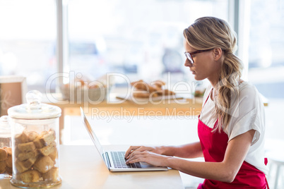 Waitress sitting at table and using laptop