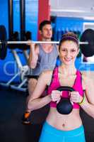 Portrait of smiling woman holding kettlebell with man lifting weights