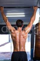 Rear view of shirtless athlete doing chin-ups