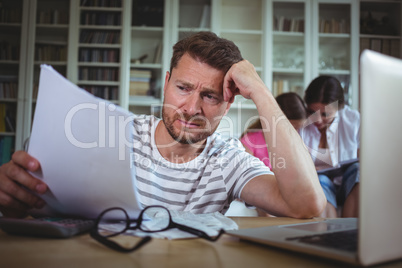 Worried man calculating bills while his wife and daughter sitting on sofa