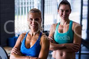 Portrait of cheerful female friends with arms crossed in gym