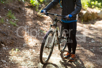 Female biker standing with mountain bike on dirt track