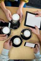 Friends using mobile phone and digital tablet while having cup of coffee