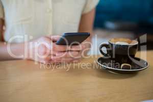 Woman using mobile phone with coffee cup on table