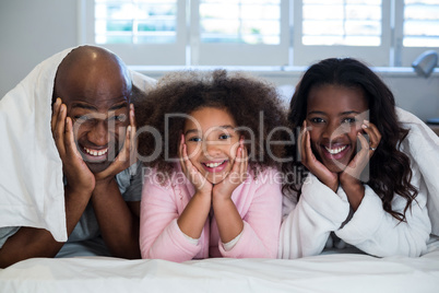 Family with hands on face lying on bed
