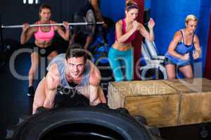 Portrait of smiling man lifting tire in gym