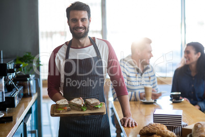 Portrait of waiter holding a sandwich on chopping board