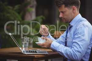 Handsome businessman having tea while using laptop