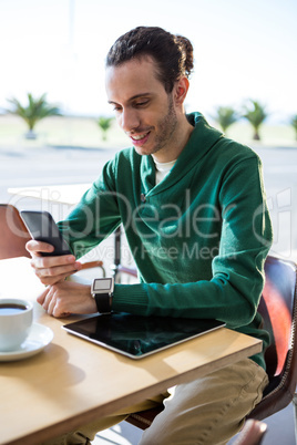 Man using mobile phone with digital tablet and cup of coffee on table