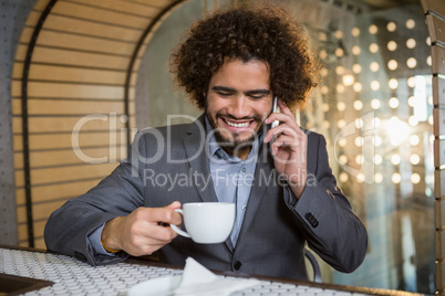 Businessman talking on mobile phone while having cup of tea