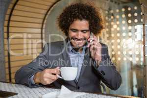 Businessman talking on mobile phone while having cup of tea