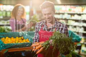 Smiling staff holding bunch of carrots in organic section