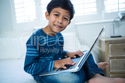 Boy using laptop while relaxing on bed