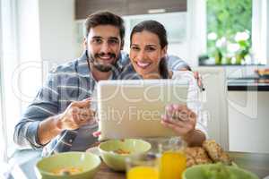 Couple using digital tablet while having breakfast at home