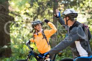 Biker couple giving high five while riding bicycle in the forest