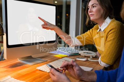 Businesswoman and colleague interacting while working on computer at their desk