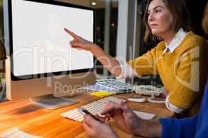 Businesswoman and colleague interacting while working on computer at their desk