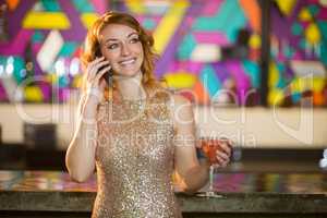 Young woman talking on mobile phone while having cocktail at counter