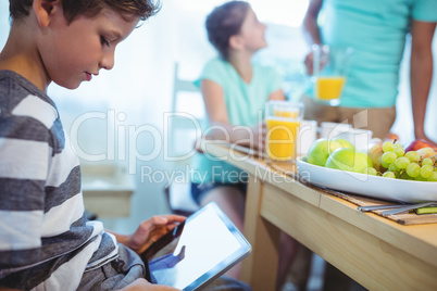 Boy using digital tablet with breakfast on table