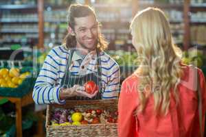 Male staff assisting woman in selecting fresh vegetables