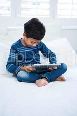 Boy using digital tablet while relaxing on bed