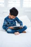 Boy using digital tablet while relaxing on bed