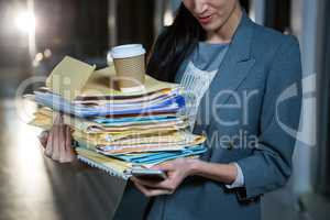 Businesswoman carrying stack of file folders while using mobile phone