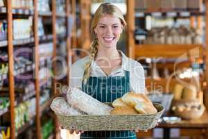 Smiling female staff holding basket of bread at bread counter