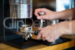 Waiter using a tamper to press ground coffee into a portafilter