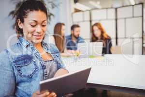 Businesswoman using digital tablet against coworkers