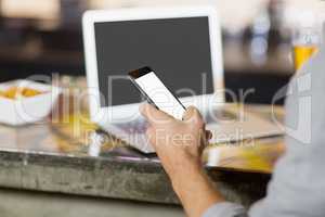 Man using mobile phone with laptop on table at bar counter