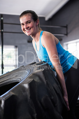 Portrait of smiling female athlete pushing tire in gym